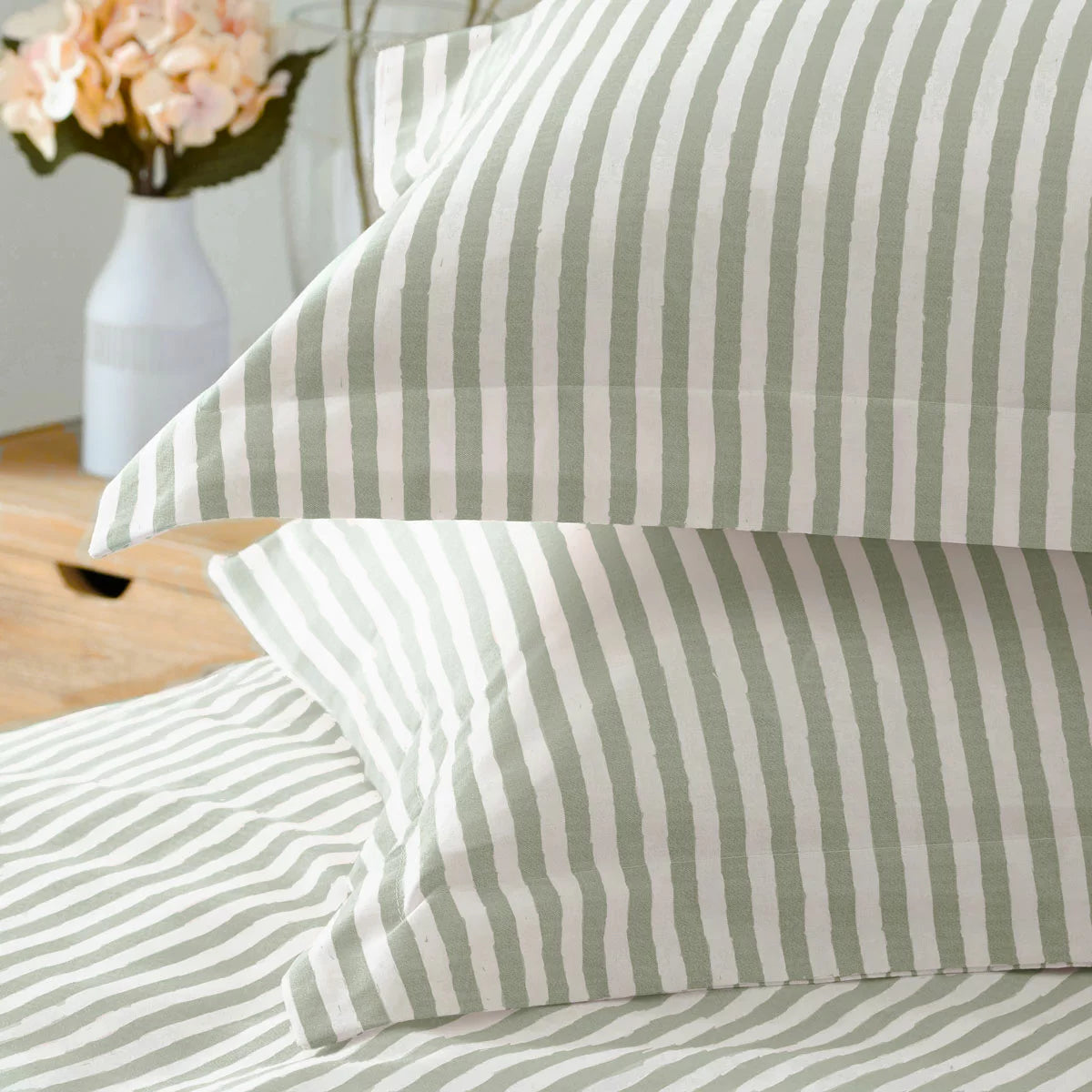 Vertical view of a single bed styled with the green and white striped Yard Hebden cotton duvet cover, displaying the reversible side folded down in a bright, modern bedroom.
