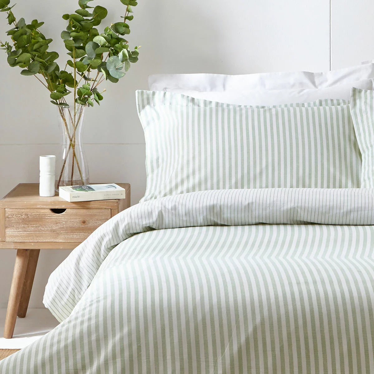 Vertical view of a single bed styled with the green and white striped Yard Hebden cotton duvet cover, displaying the reversible side folded down in a bright, modern bedroom.