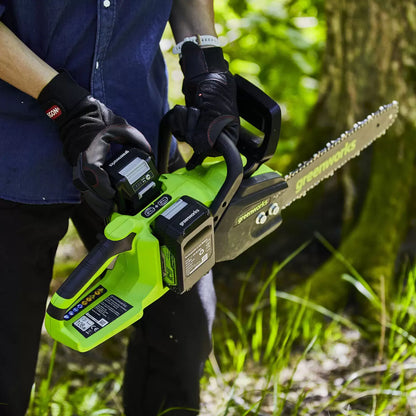 Greenworks 48V cordless brushless chainsaw with dual batteries cutting tree branches during garden maintenance