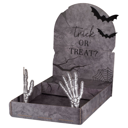 Front angle view of a grey cardboard tombstone treat stand displaying Halloween cupcakes on a dark party table.