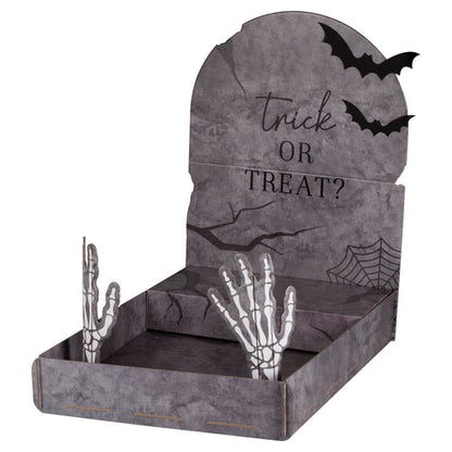 Front angle view of a grey cardboard tombstone treat stand displaying Halloween cupcakes on a dark party table.