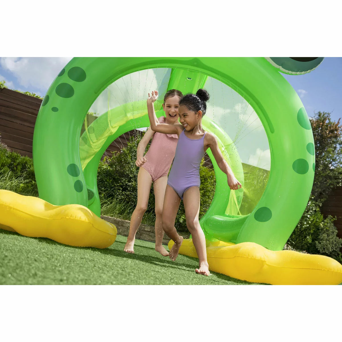 Giant green inflatable frog-shaped sprinkler arch tunnel spraying water onto a green garden lawn during sunny outdoor play.
