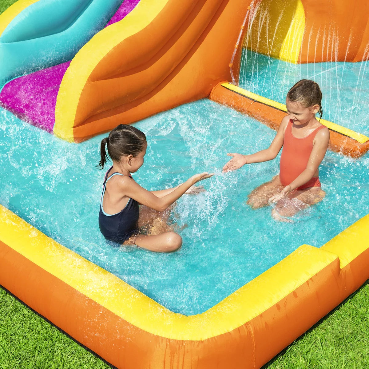 H2OGO! Tidal Tower orange inflatable mega water park with climbing tower, water slide, splash pool, crawl-through tunnel, sprinkler wall, and dump bucket set up in a sunny family garden-2