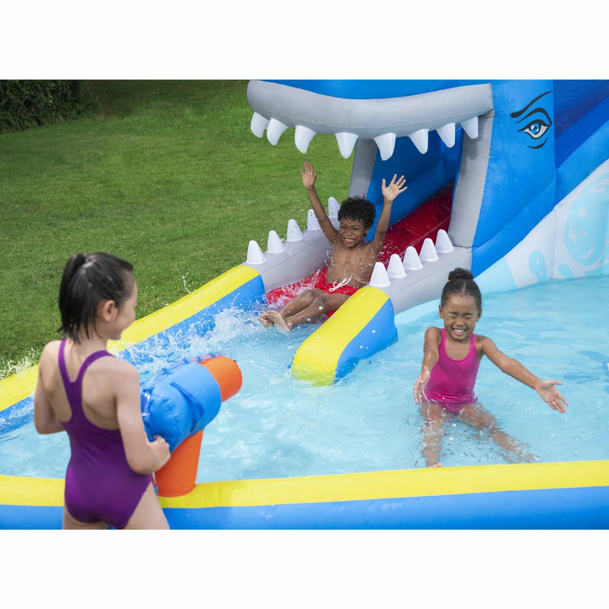 H2OGO! Whales 'n Waves blue inflatable kids water park with whale-themed slide, climbing wall, splash pool, built-in water sprayers, and interactive water blasters set up in a sunny garden-2