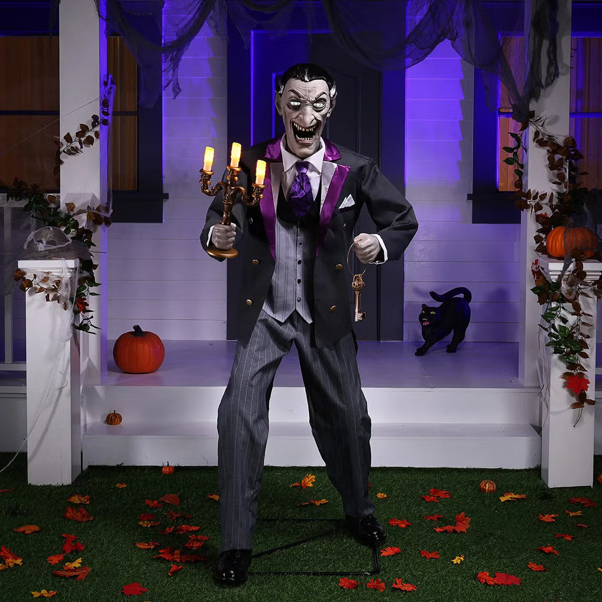 Full-length shot of a 6ft tall animated Halloween butler prop in a black suit holding an illuminated candelabra on a foggy front porch at dusk.