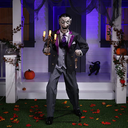 Full-length shot of a 6ft tall animated Halloween butler prop in a black suit holding an illuminated candelabra on a foggy front porch at dusk.
