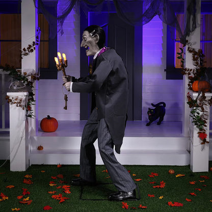 Full-length shot of a 6ft tall animated Halloween butler prop in a black suit holding an illuminated candelabra on a foggy front porch at dusk.