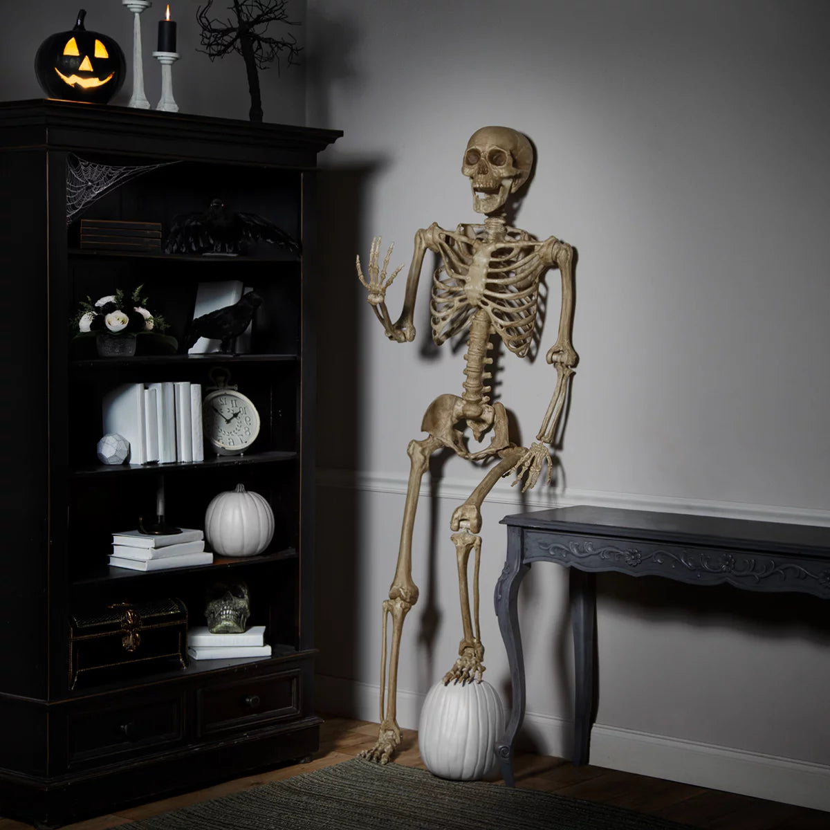 Full-length front view of a realistic 7ft natural bone-colored poseable skeleton standing against an indoor neutral wall.