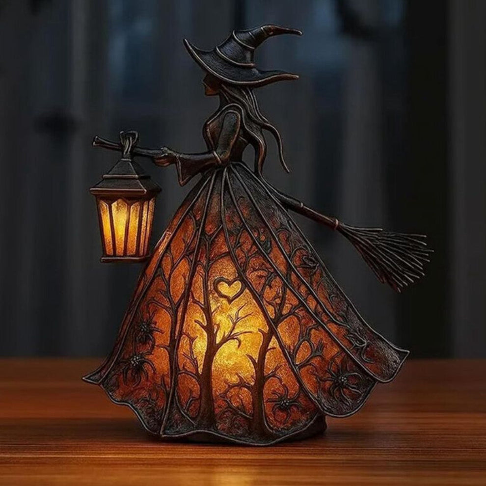 A detailed black resin Halloween gothic witch table lamp holding a glowing lantern on a dark wooden surface.