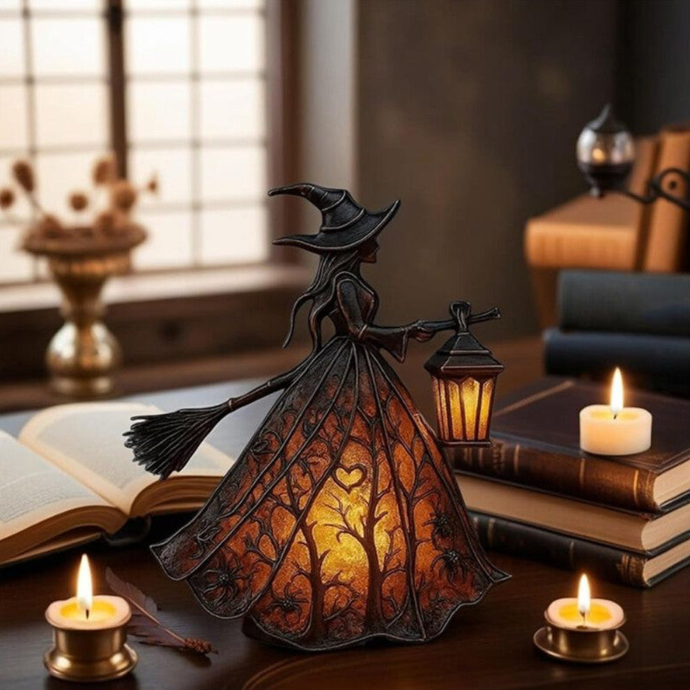 A detailed black resin Halloween gothic witch table lamp holding a glowing lantern on a dark wooden surface.