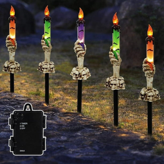 A 5-pack of Halloween lighted skeleton hand candle stakes glowing with warm white LEDs along a spooky outdoor garden lawn