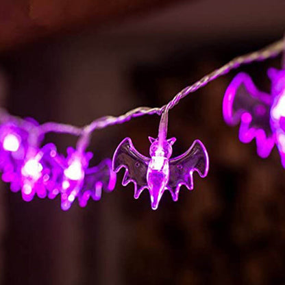 A 19.7ft multi-color Halloween string light featuring pumpkin, bat, and ghost motifs glowing brightly along an outdoor porch railing.