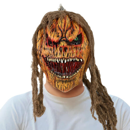 Close-up of a detailed orange and black scary full-face pumpkin mask with dark eye sockets worn against a dark studio background.