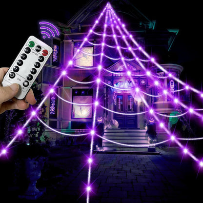Giant 16-foot purple LED illuminated spider web drapes down a front yard lawn staked into ground at dusk.