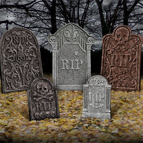 Five weathered gray foam Halloween tombstones of varying heights arranged on a green grassy lawn at dusk.