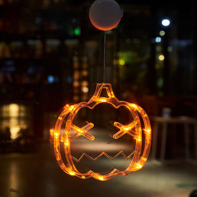 An illuminated Halloween window LED light with a suction cup glowing brightly against a glass pane at night.