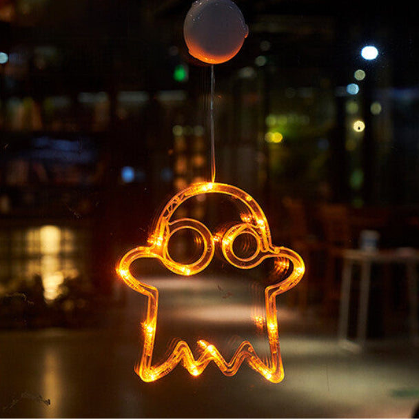 An illuminated Halloween window LED light with a suction cup glowing brightly against a glass pane at night.