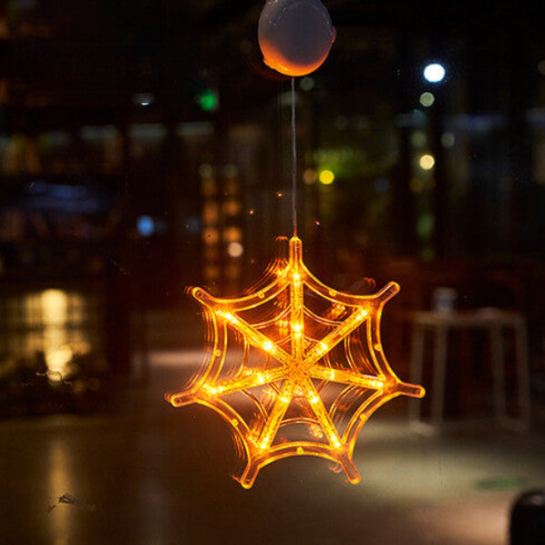 An illuminated Halloween window LED light with a suction cup glowing brightly against a glass pane at night.