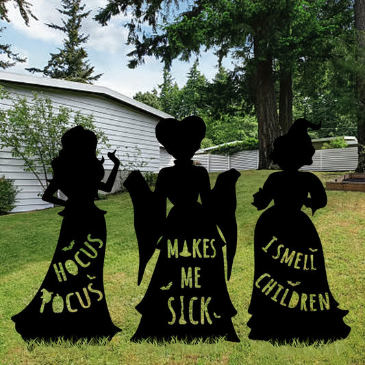 Three black plastic witch silhouette yard signs anchored into green grass with ground stakes under dusk lighting.