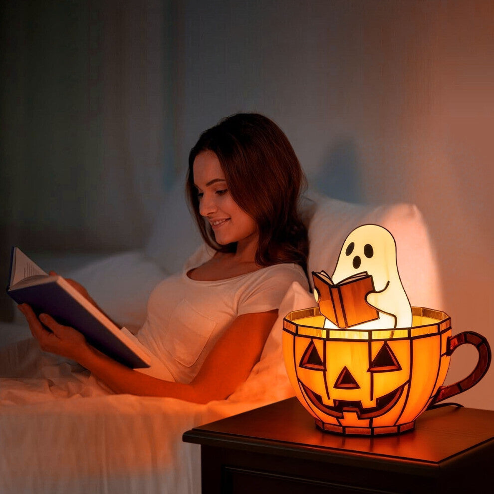 A handmade ghost reading a book lamp glowing with soft color-changing light on a wooden bookshelf decorated for Halloween.
