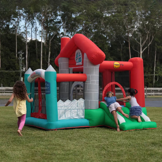 Colourful Happy Hop inflatable bouncy castle with integrated slide and enclosed ball pit set up on a green garden lawn during outdoor family play.