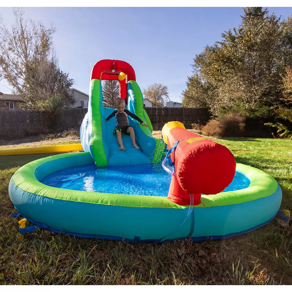 Colourful Happy Hop inflatable water slide pool with climbing wall, bounce area, splash pool and water cannon set up on a sunny garden lawn for children's outdoor summer play.