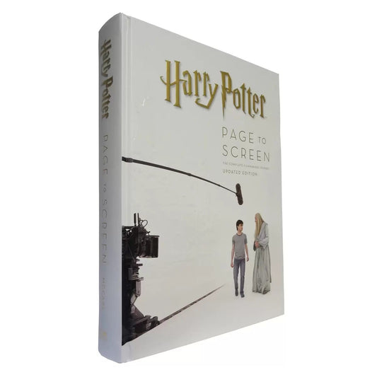 Open hardcover book Harry Potter Page to Screen showing detailed concept art, film stills, and text on a dark wooden desk.