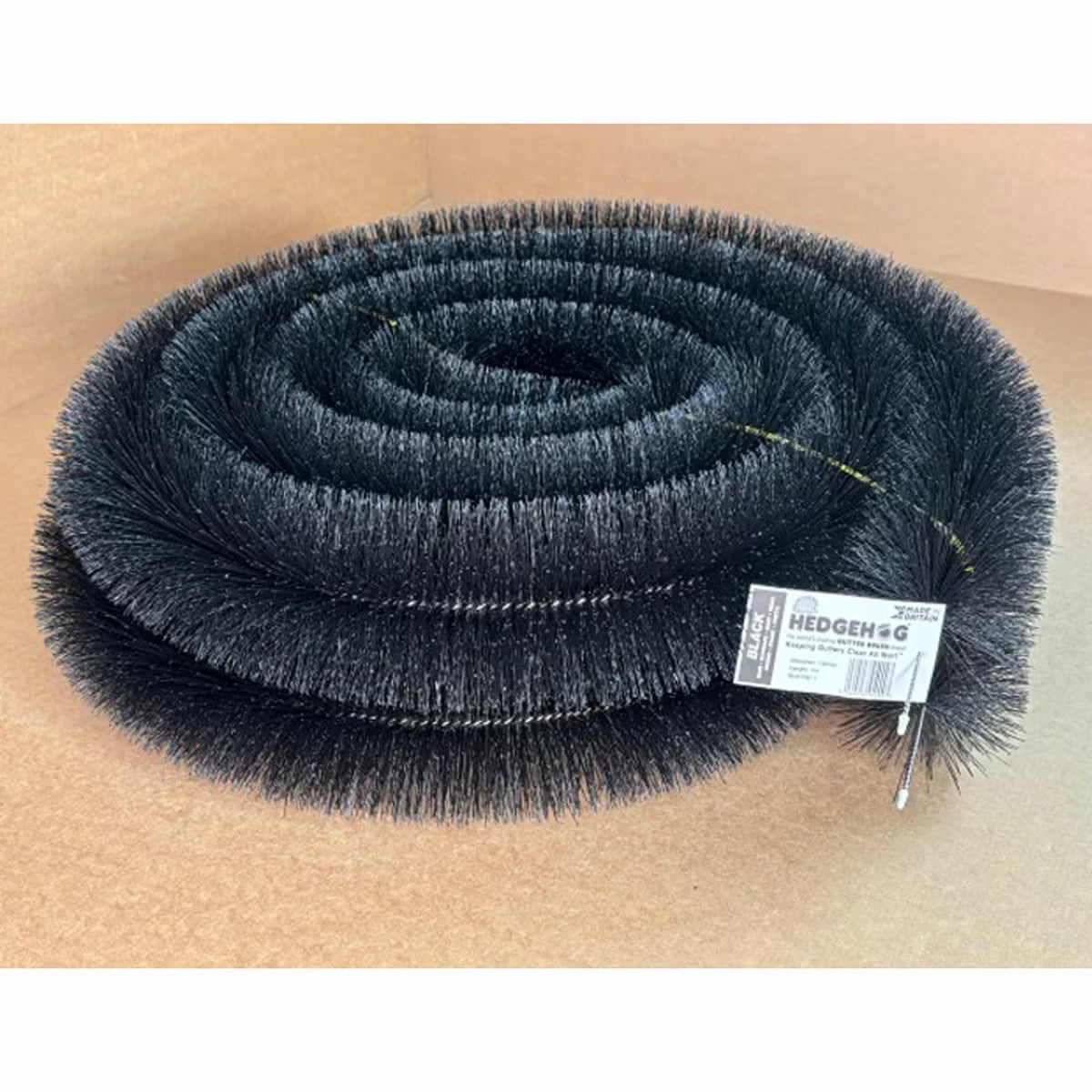 Black cylindrical polypropylene Hedgehog gutter brush guard displaying stiff radial bristles and wire central core laid inside a white plastic house gutter.