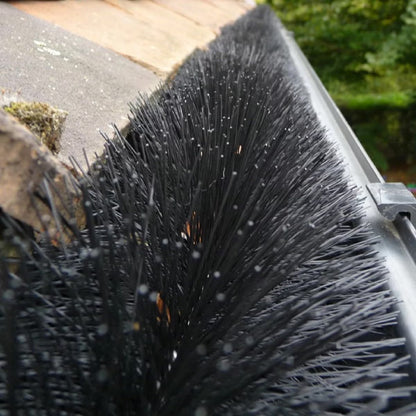 Black cylindrical polypropylene Hedgehog gutter brush guard displaying stiff radial bristles and wire central core laid inside a white plastic house gutter.