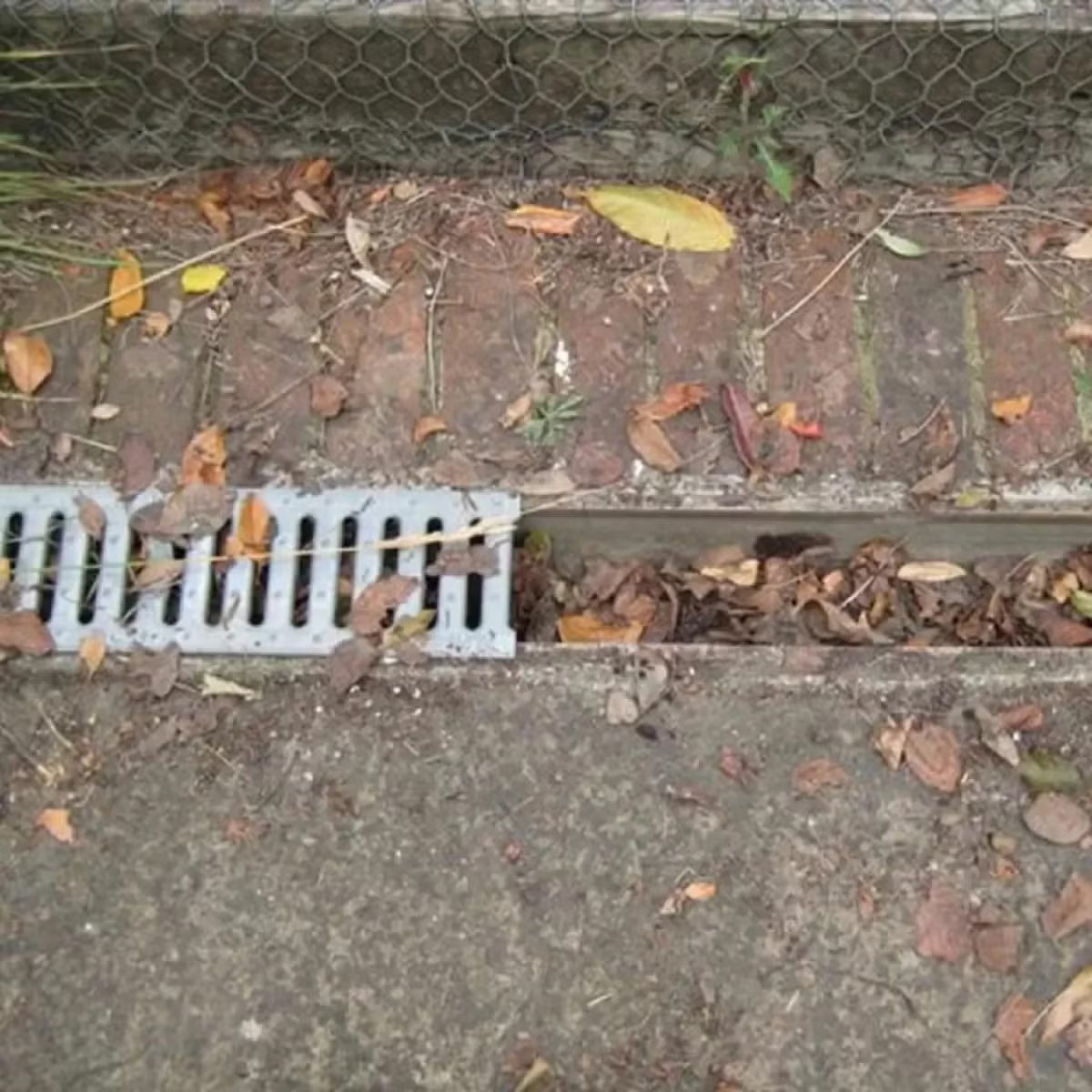Black cylindrical polypropylene Hedgehog gutter brush guard displaying stiff radial bristles and wire central core laid inside a white plastic house gutter.