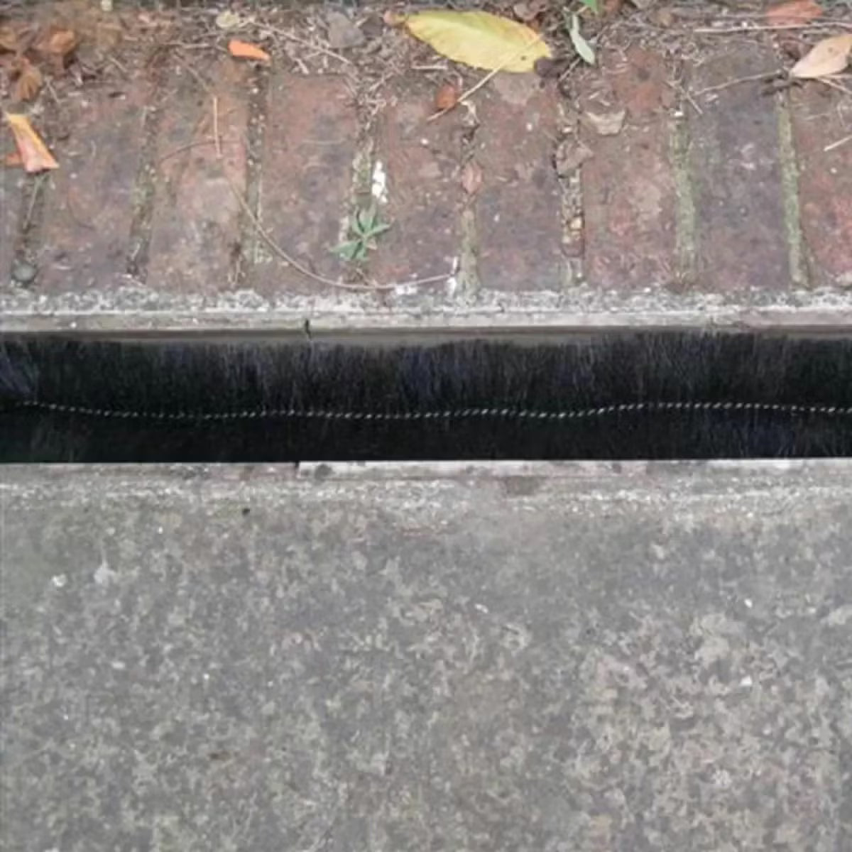 Black cylindrical polypropylene Hedgehog gutter brush guard displaying stiff radial bristles and wire central core laid inside a white plastic house gutter.