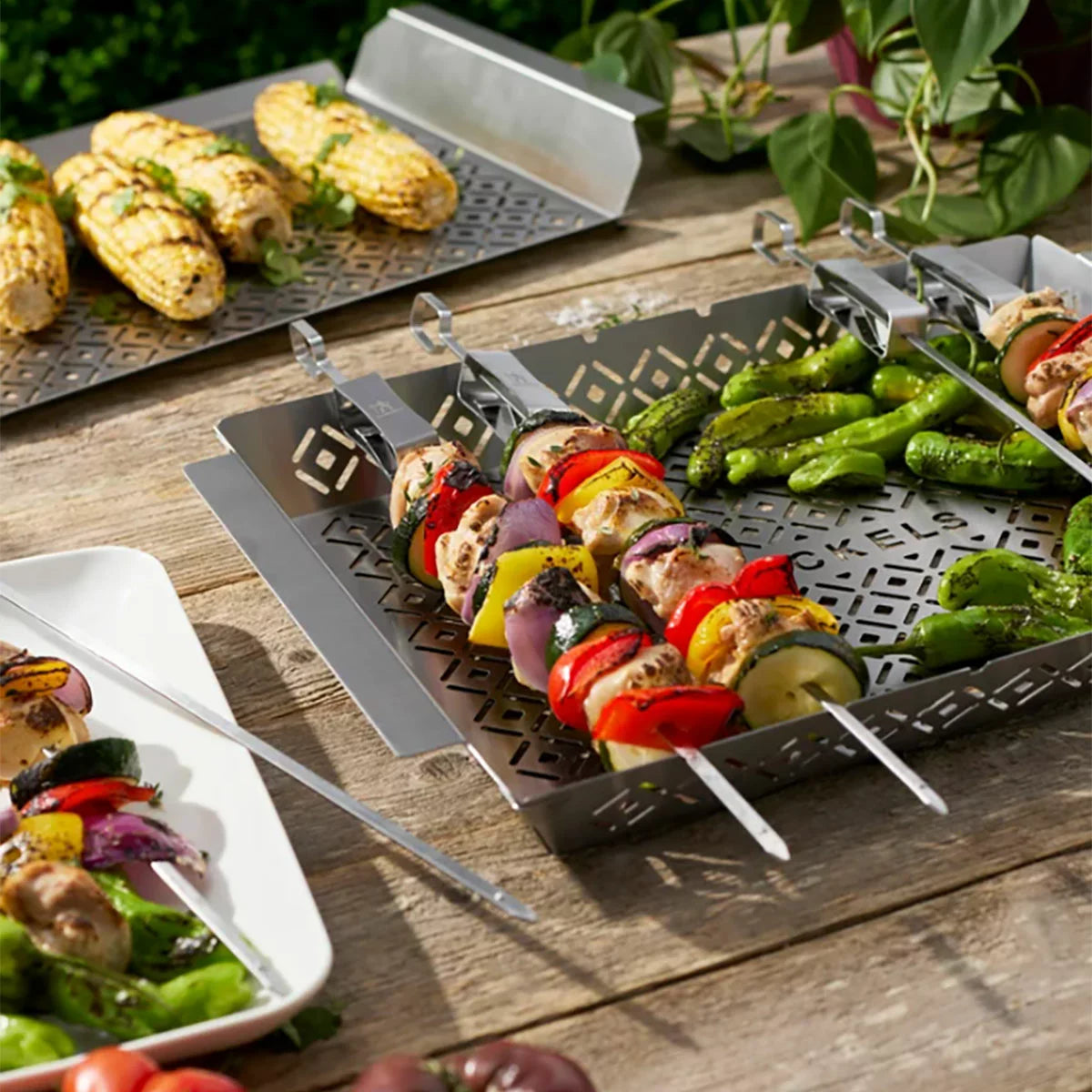 A Henckels 8-piece BBQ set laid out on a clean grilling station, showing the stainless steel grill basket, large grill topper tray, and six skewers with release sliders.