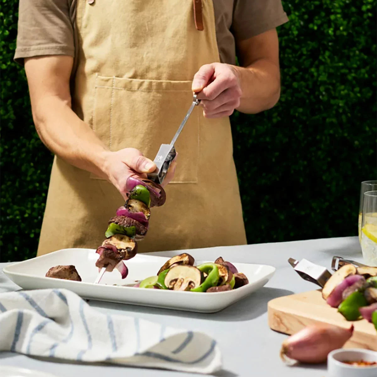 A Henckels 8-piece BBQ set laid out on a clean grilling station, showing the stainless steel grill basket, large grill topper tray, and six skewers with release sliders.