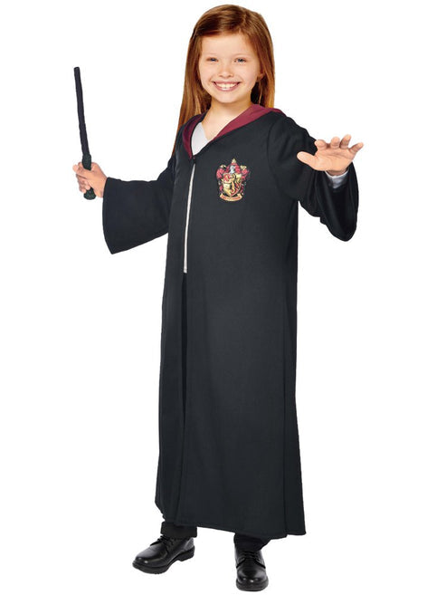 Child wearing an ankle-length black Hermione robe with red hood lining and Hogwarts crest holding a magical wand against a plain backdrop.