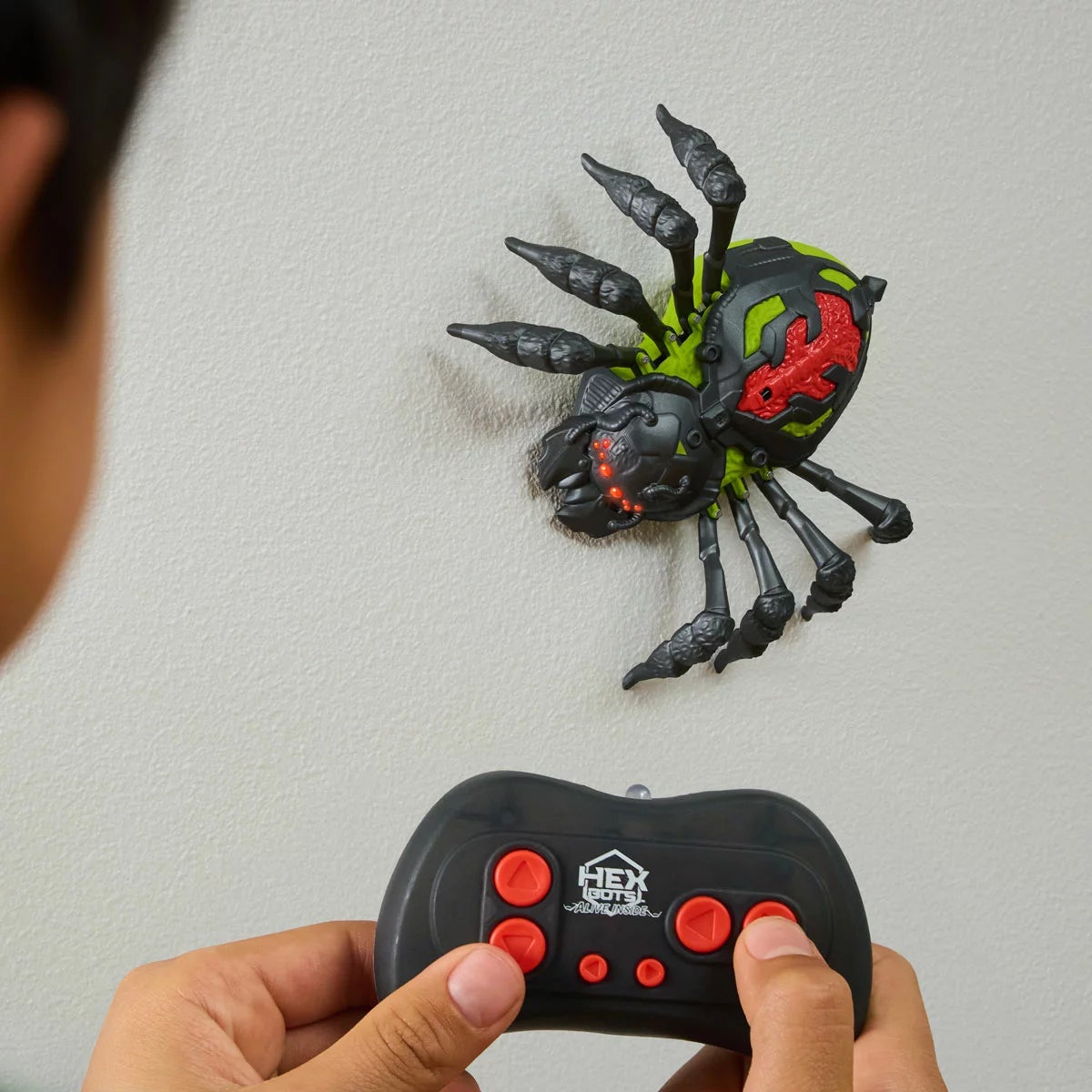 Black Hex-Bots crawling wall spider toy with glowing red LED eyes and furry texture climbing up a white wall.