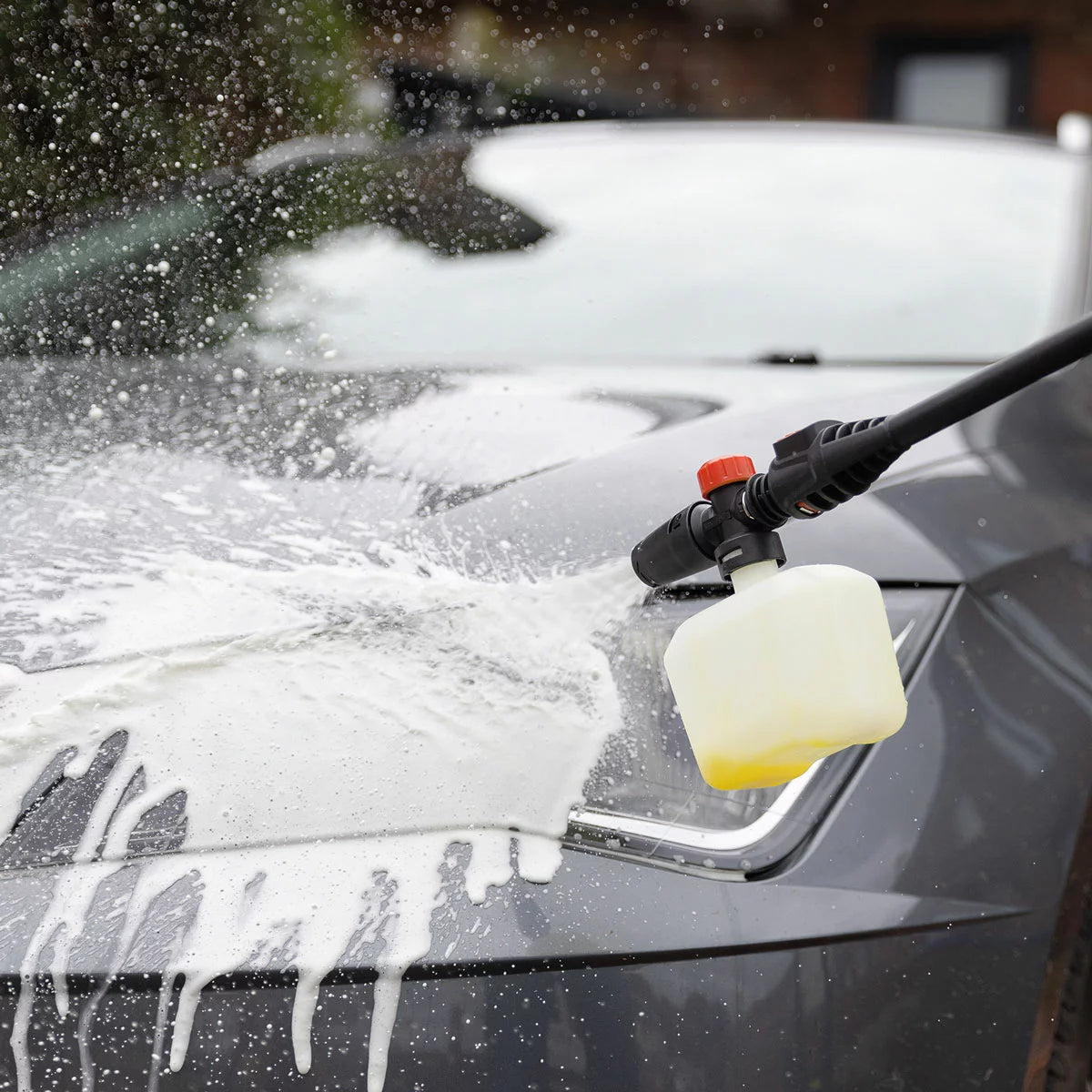 A compact Hilka 1600W pressure washer shown with its patio cleaner attachment, high-pressure nozzle, and foam bottle, set against a clean residential driveway.