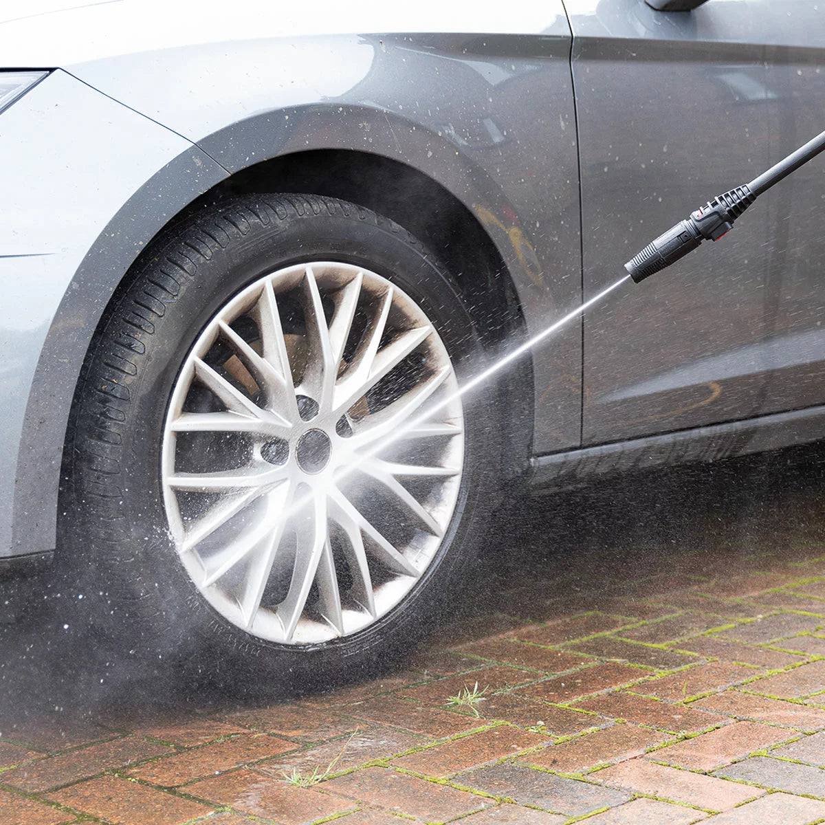 A compact Hilka 1600W pressure washer shown with its patio cleaner attachment, high-pressure nozzle, and foam bottle, set against a clean residential driveway.