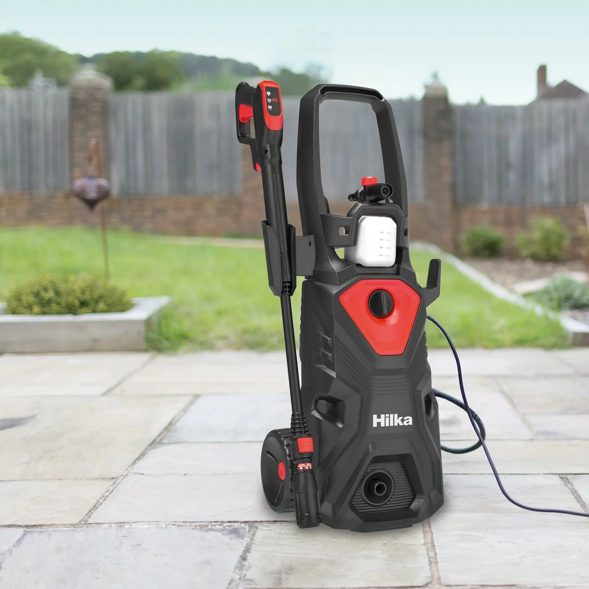 A Hilka 2,000W pressure washer set up on a residential driveway, with various attachments including the patio cleaner and foam bottle neatly arranged nearby.