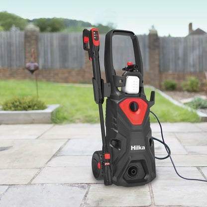 A Hilka 2,000W pressure washer set up on a residential driveway, with various attachments including the patio cleaner and foam bottle neatly arranged nearby.