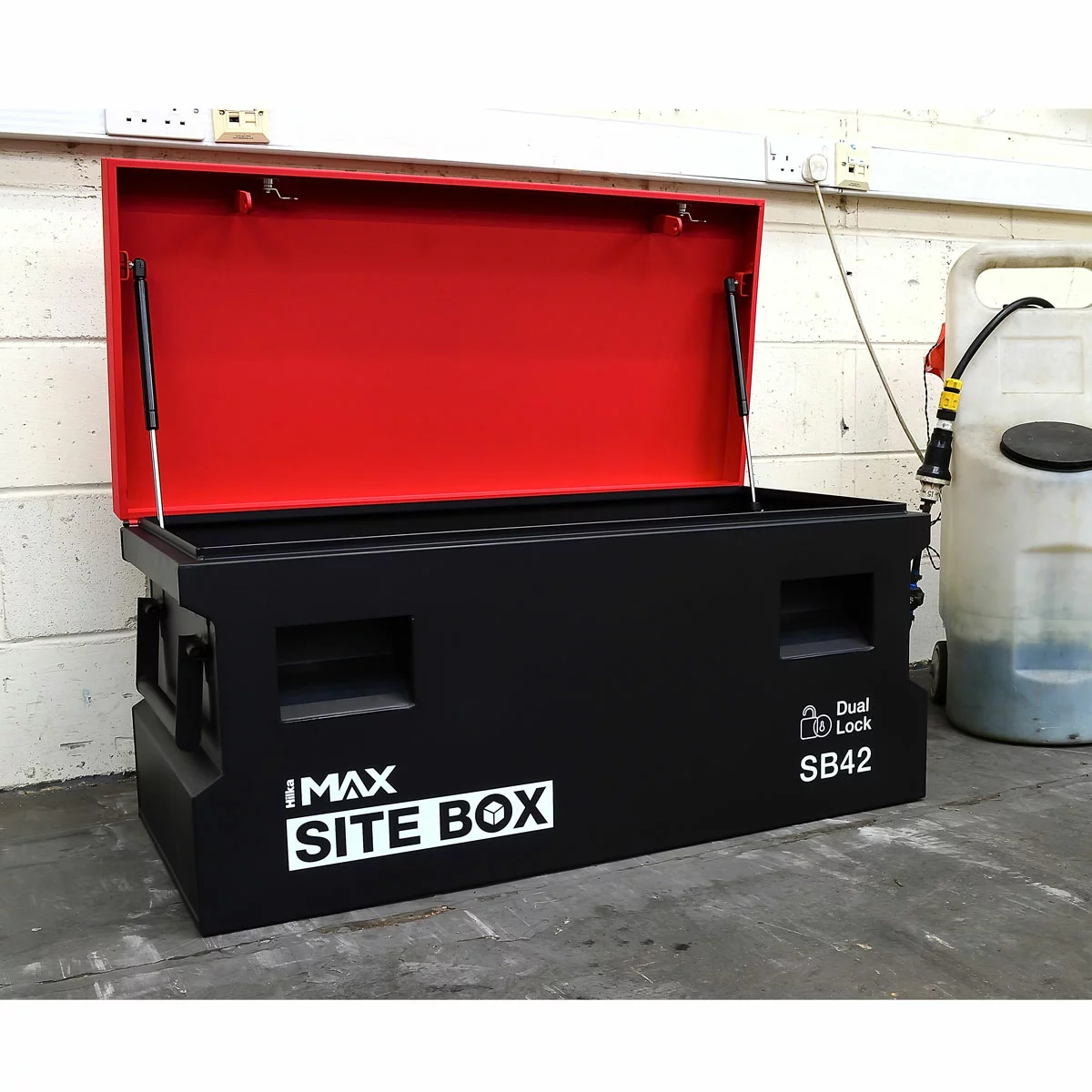 Heavy-duty industrial grey Hilka 42-inch steel site storage box with its lid open, showing gas struts and recessed lock pocket on a concrete floor.