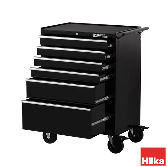 Front angle view of the black Hilka HD Pro+ 6-drawer steel tool trolley on rubber castors with drawers slightly open to show the silver aluminium pulls and black foam liners in a professional workshop environment.