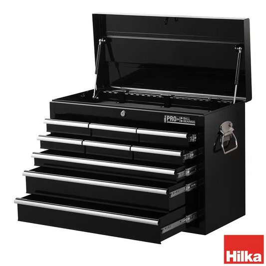 Black steel Hilka HD Pro+ 9-drawer tool chest shown from a three-quarters angle with the top lid open on dual gas struts, showcasing the aluminium drawer pulls and red interior details on a rustic wooden workbench.