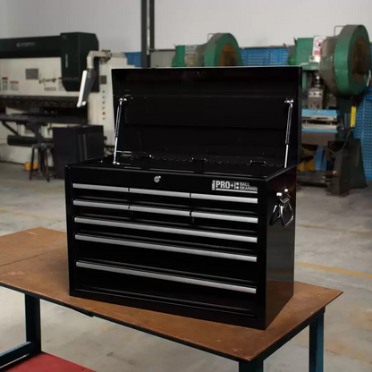Black steel Hilka HD Pro+ 9-drawer tool chest shown from a three-quarters angle with the top lid open on dual gas struts, showcasing the aluminium drawer pulls and red interior details on a rustic wooden workbench.