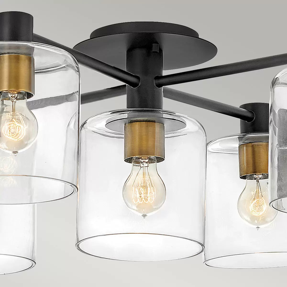 Hinkley Quintiesse Axel five-light semi-flush ceiling chandelier in matte black steel and heritage brass accents featuring clear glass globes mounted on a low ceiling.