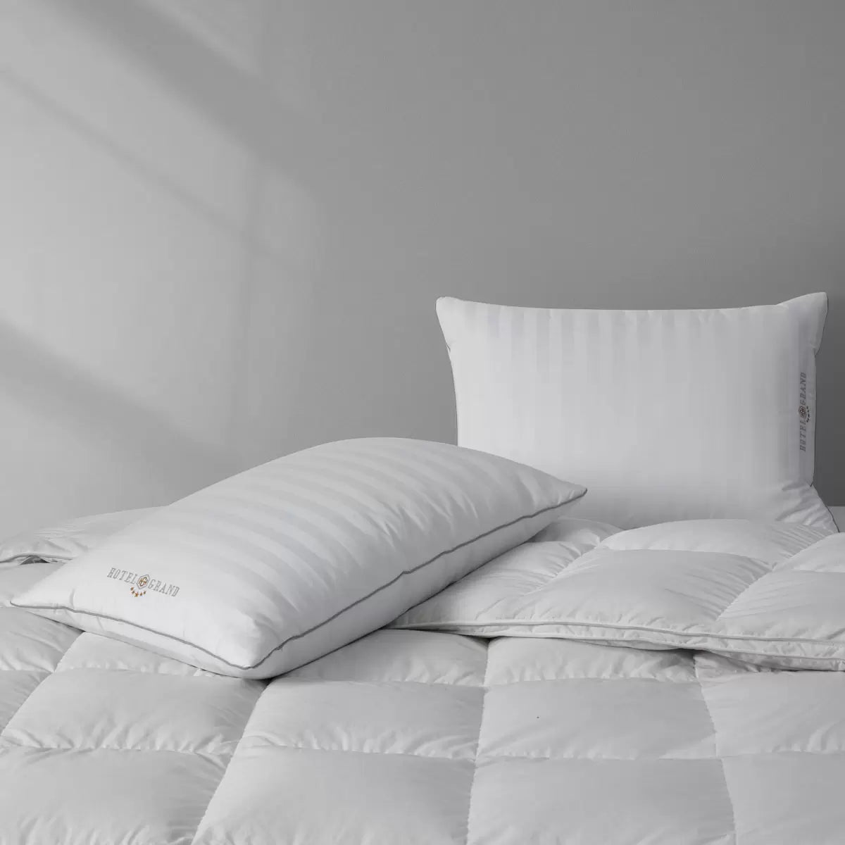 Hotel Grand Feather & Down Rolled Pillow 2 pack styled elegantly on a crisp white bed with silver piping details