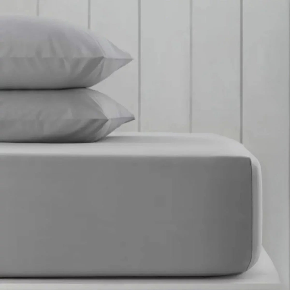 A pack of two neatly folded double-sized Hotel Signature cotton sateen fitted sheets showing the thick elastic corner grip on a clean bed.