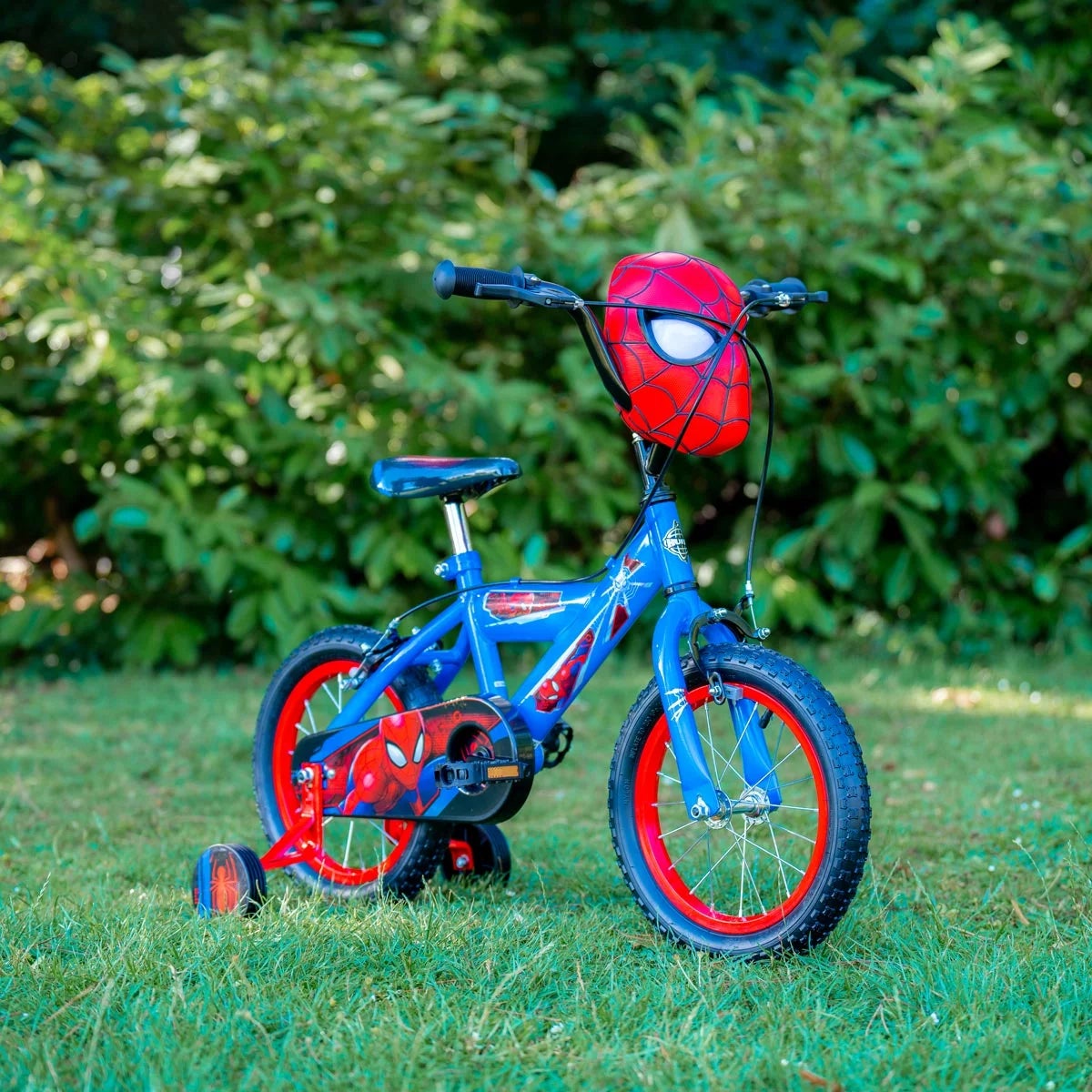 Side view of the Huffy Spider-Man 14-inch kids bike featuring a red and blue steel frame with Spider-Man graphics resting on a paved park path.