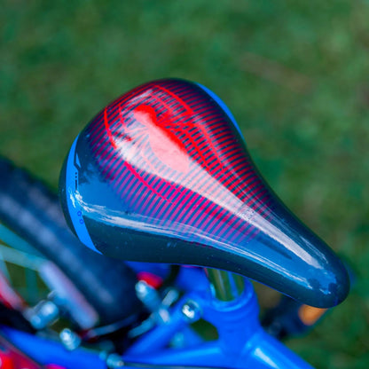 Side view of the Huffy Spider-Man 14-inch kids bike featuring a red and blue steel frame with Spider-Man graphics resting on a paved park path.