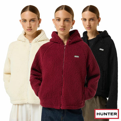 Side angle view of a woman wearing a beige Hunter Women's Highland Hooded Fleece with plush borg texture and a zip-up hood outdoors.