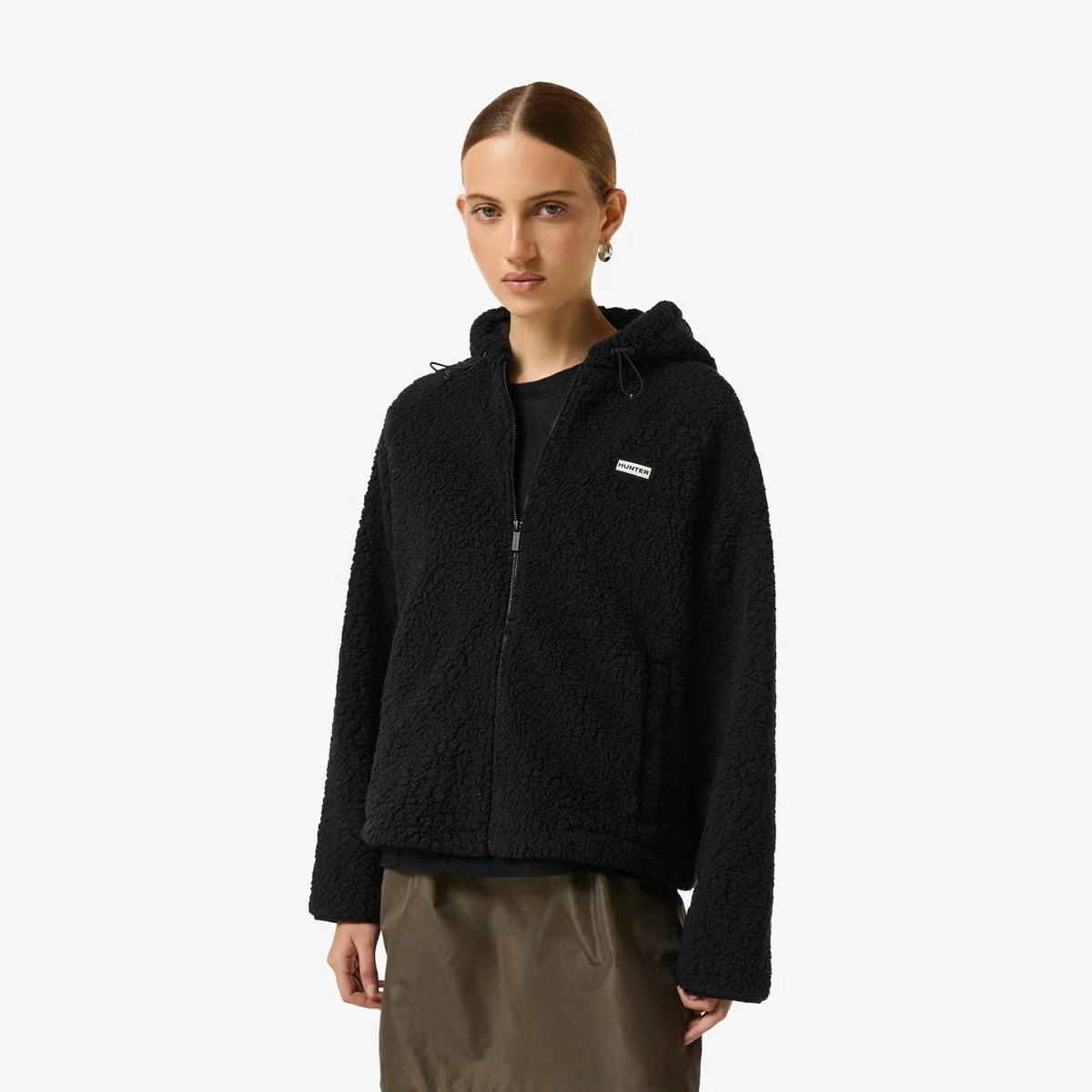 Side angle view of a woman wearing a beige Hunter Women's Highland Hooded Fleece with plush borg texture and a zip-up hood outdoors.